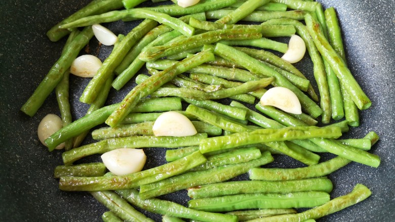 豆角烧茄子(少油健康版),将豆角和蒜煸炒至外表变焦黄。