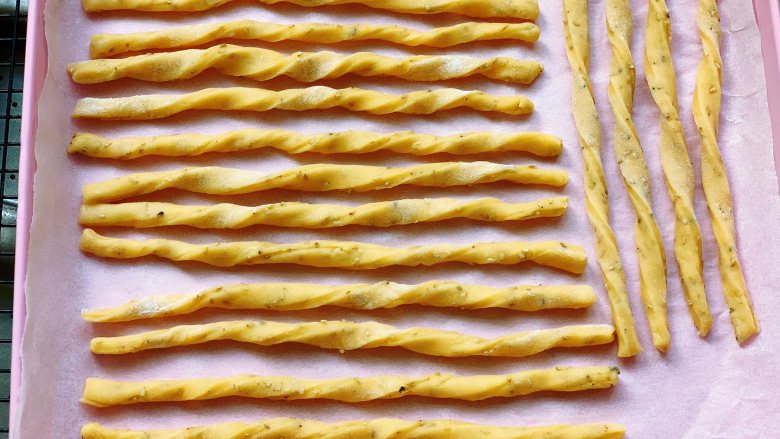 西红柿磨牙棒,两手拿起一根长条的两端，朝相反的方向扭几圈，直接放入铺了油纸的烤盘里，间距不要挨得太近。