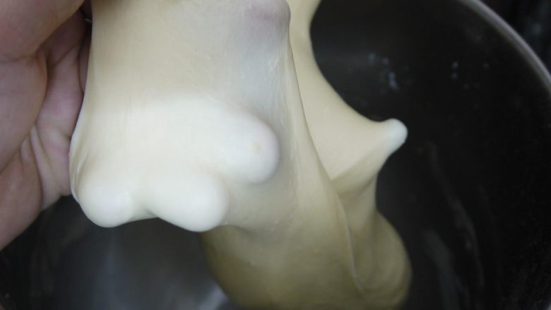 港式肠仔面包,开启厨师机,先用低速将材料混合,然后转中速揉至面团光滑不粘手,面团能拉出较厚的膜。