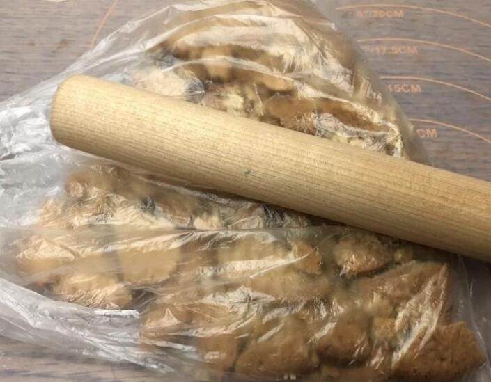 百香芒果双层生乳酪蛋糕(免烤箱),饼乾装入塑胶袋中,用桿麵棍压至细碎状。
