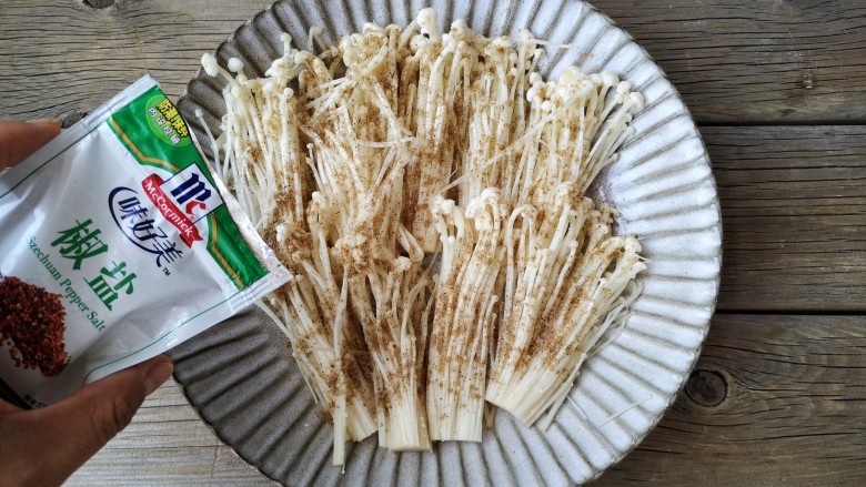 椒盐金针菇,将处理好的金针菇平铺在盘中,均匀撒上适量的椒盐,如果有时间可以腌制10分钟,没时间就接着进行下面的操作即可。