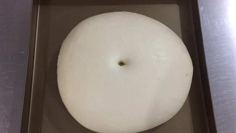花环面包,将揉好的面团稍微整圆,放入容器内,盖上保鲜膜进行第一次发酵。发酵温度室温27度,发酵至原来的两倍大。发酵好的面团,手指粘粉在面团中心戳一个洞,面团不会回缩就是发酵好了。