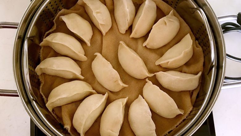东北酸菜饺子,把包好的蒸饺放入笼屉,冷水上屉,放入蒸锅