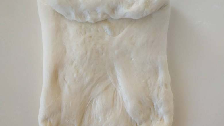 北海道牛奶土司,１１、将面团分成２块，用手压扁，翻面后从上往下卷起，不用卷太多。
