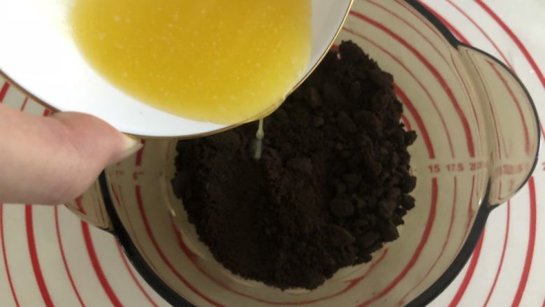 胜过冰淇淋蛋糕的「奥利奥冻芝士蛋糕」,这个时候黄油差不多已经融化好了,将融化的黄油倒入180g饼干碎里,搅拌均匀。