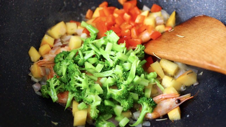 苹果北极虾时蔬炒饭,大火继续翻炒至所有的食材后,加入焯过水的西兰花和红椒丁,大火继续翻炒均匀。