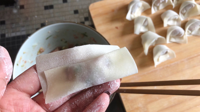鲜香馄饨,把肉馅从底部慢慢卷起来,留一指空的距离,用筷子沾一点水抹在一侧。