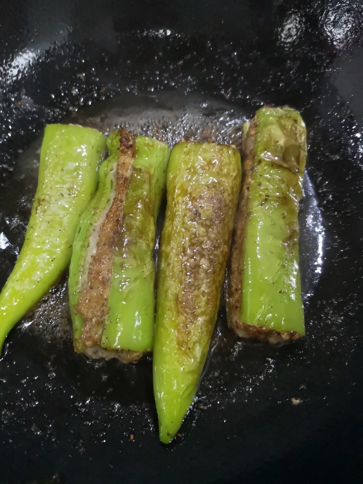 青椒酿肉,锅里倒进适量油,放进塞好肉馅的青椒小火煎,一点要小火耐心煎,这样青椒的辣味会慢慢渗入肉馅里,也能把肉馅煎大半熟了