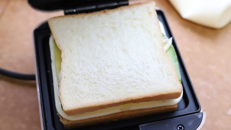 牛油果鸡蛋三明治,然后在表面再盖一层吐司面包。把面包和食材对整齐，用手顺带着扶一下吐司面包，把三明治机的盖子扣上，加热两三分钟就可以。