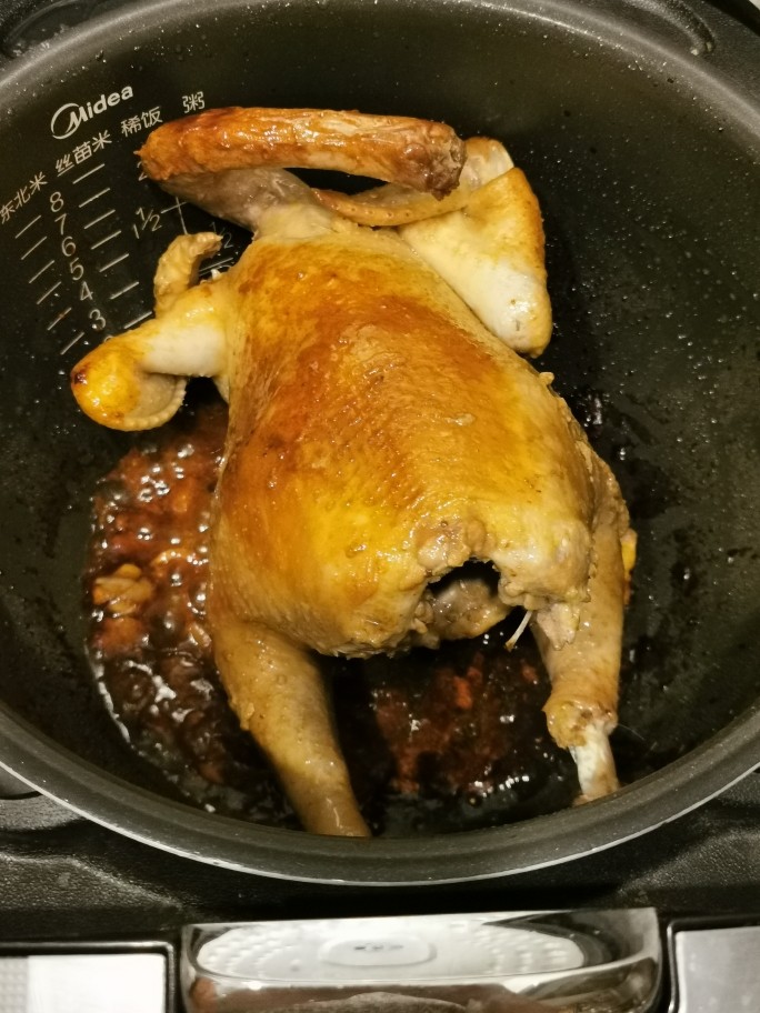 香飘满屋电饭锅鸡(简单版),电饭锅按煮饭键,下小许油,姜蒜垫底,鸡肚子里放姜葱,摆入锅盖上,腌鸡的酱汁同时加入,水不用放。20分钟左右,翻转鸡身,这样整鸡受热均匀,上色漂亮。