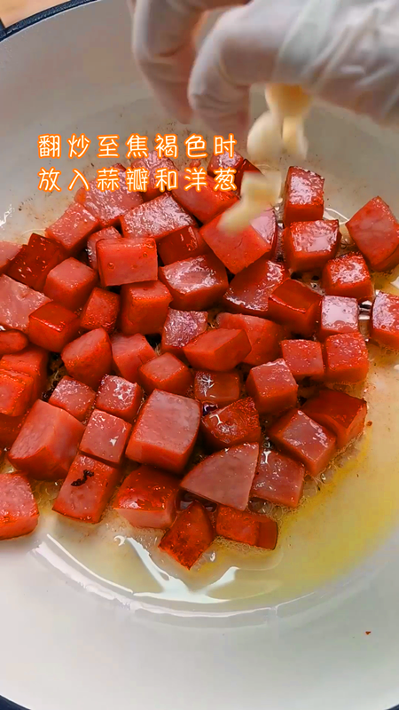 加拿大火腿焖土豆,先加入加拿大火腿，翻炒至有焦褐色时加入蒜瓣和洋葱