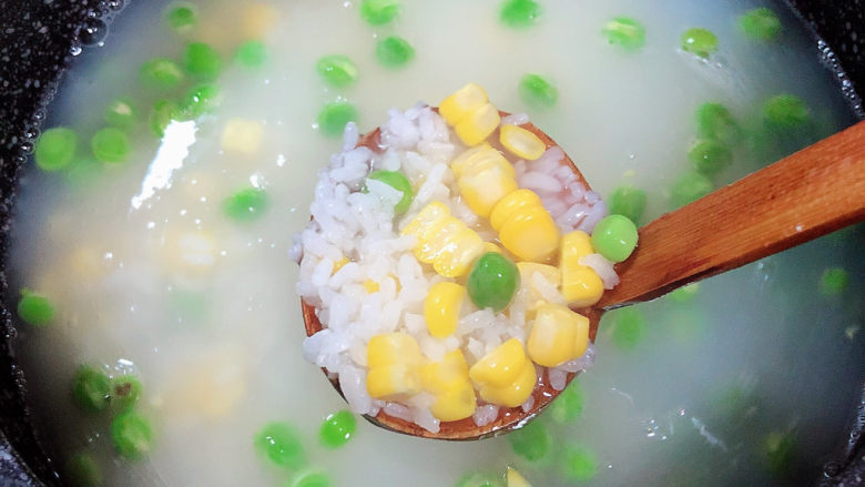 冬日暖心菜 扇贝田园砂锅粥,粥煮至7成熟时,加入豌豆和玉米粒,搅拌均匀,继续小火熬煮。