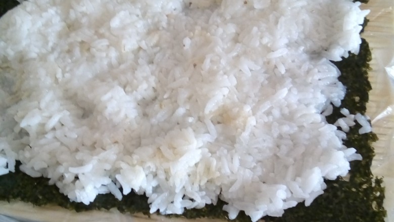寿司,在寿司帘铺上海苔再铺上米饭,为不沾手沾点水