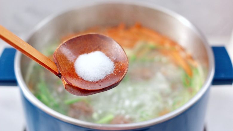 冬日暖心菜 手工牛肉丸子粉丝双色萝卜煲,大火煮沸后,看见青萝卜和胡萝卜丝断生变色的时候,加入适量的盐调味。