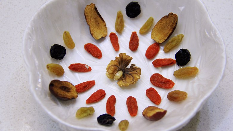 香糯可口八宝饭,在深碗中先铺一层保鲜膜,然后按喜好把干果类摆好,因为最后的成品需要翻转倒置,所以干果类的较美观的一面要朝碗放置。