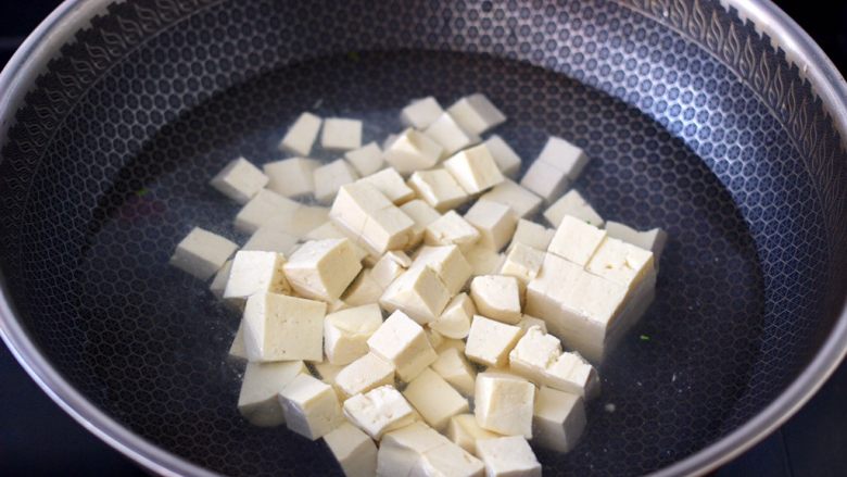 金针菇豆腐鱿鱼煲,锅中倒入适量的清水,把豆腐进行焯水,这样做出来的成品汤色清澈透亮。