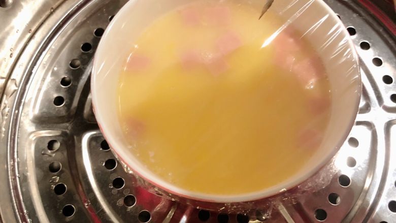 火腿蒸蛋,用保鲜膜封住蒸碗,用牙签在膜上戳细孔,轻轻戳,而后放入蒸锅中蒸熟
