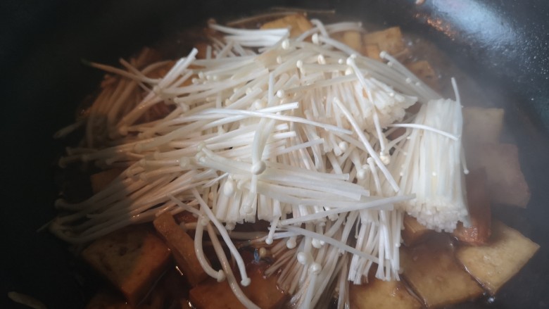 金针菇豆腐煲,锅里留少量油,放入蒜末炒香后倒入炸好的豆腐,翻炒两下倒入料汁,将金针菇放入锅里,加水炖至金针菇变色。