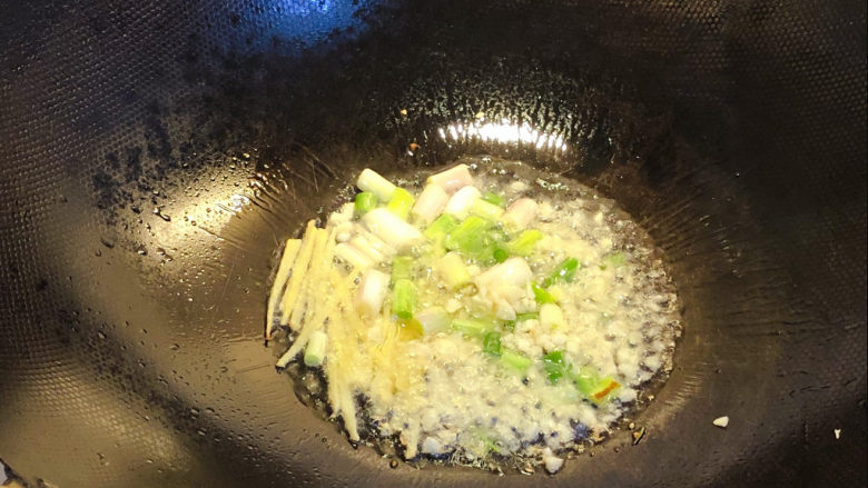 油焖大虾,锅内倒入适量油,温热后倒入葱白、蒜粒和姜丝爆香。