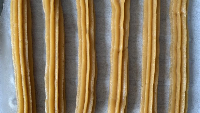 Churros~吉事果/吉拿棒/吉拿果~“西班牙油条”,在铺好油纸的烤盘上挤出约10厘米的长条,挤完一条时用刀切断。放入预热好的烤箱即可,我家是个小烤箱,一次最多只能烤6条。