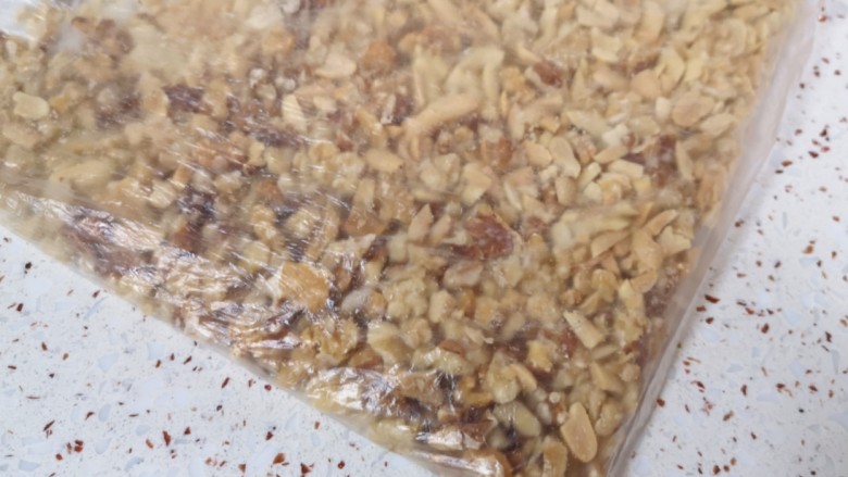 芝麻花生糖,将花生仁和核桃仁一起装进保鲜袋,用擀面杖敲成大颗粒状。