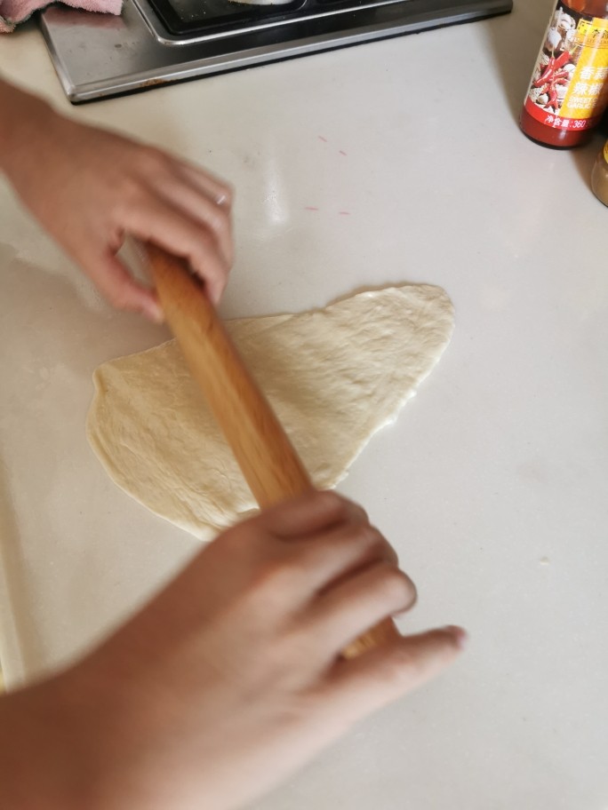 松软肠仔包【面包机发面简易版】,枱垫上涂抹点食用油，用擀面棍将小面团擀成扁扁的长条形，排走气泡，一头宽一头窄，肠仔放宽那头开始卷起。