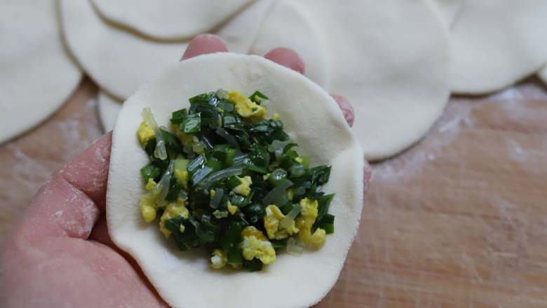 韭菜鸡蛋粉丝包子,用手掌心按一下面剂子,然后用擀面杖擀成一个圆形,中间略厚,四周略薄,包入一大勺韭菜鸡蛋馅。