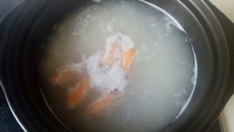 鲜虾砂锅粥,虾头放入炒锅中加入适量油炒出虾油,加入适量清水煮开,倒入砂锅中