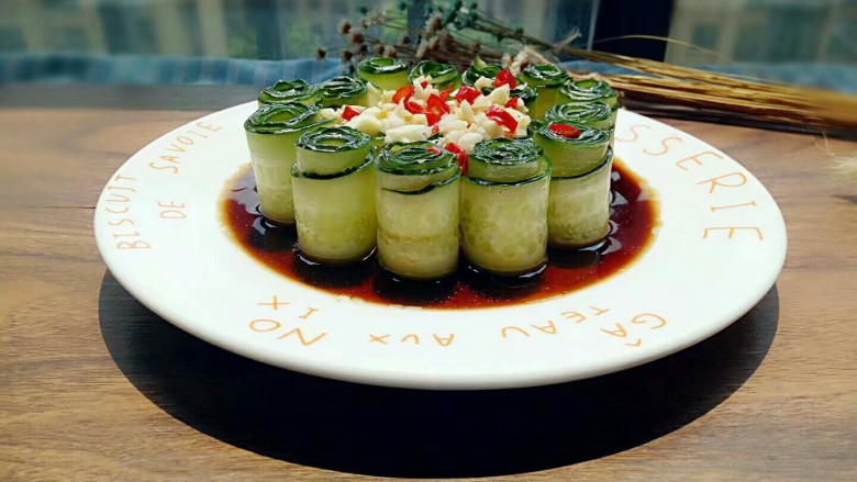 凉拌黄瓜卷,将调好的料汁浇在黄瓜上,蒜末和红辣椒段摆放在黄瓜上