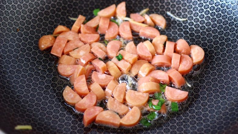 海鲜菇鸡蛋汤,锅中倒入剩下的5克花生油烧热,大火爆香葱姜后,放入火腿片大火快速翻炒至变软。