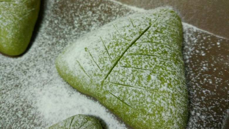 抹茶奶酪软欧面包,二次发酵好以后撒一层干粉,网筛一定要拿的高一点,轻抖,太低面粉就会落成一坨,撒面粉薄薄一层就可以了。然后用刀片割出纹路,没有刀片用锋利一点的刀,割的时候一刀成型,不要来回像拉大锯一样,这样的纹路不会好看的。
