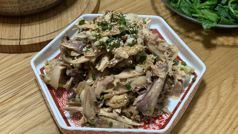 盐焗手撕鸡,稍凉一点的时候,顺着鸡架撕成小块,放入锅底的鸡汁,撒上葱花和炒香的白芝麻拌匀