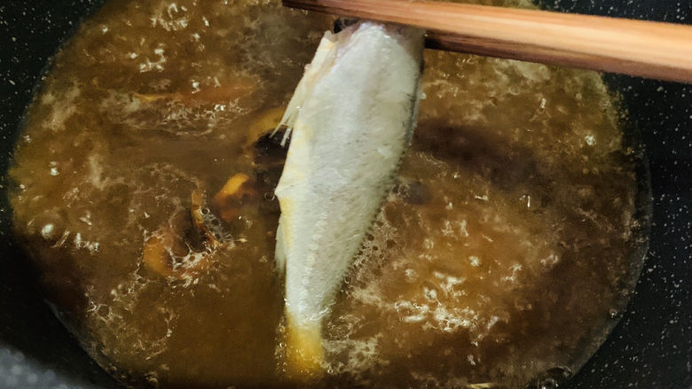 红烧小黄鱼,汤汁煮沸时,用筷子夹入小黄鱼;