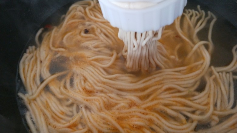 麻辣牛肉面,锅中倒入适量水烧开,面团装入压面器压出面条。