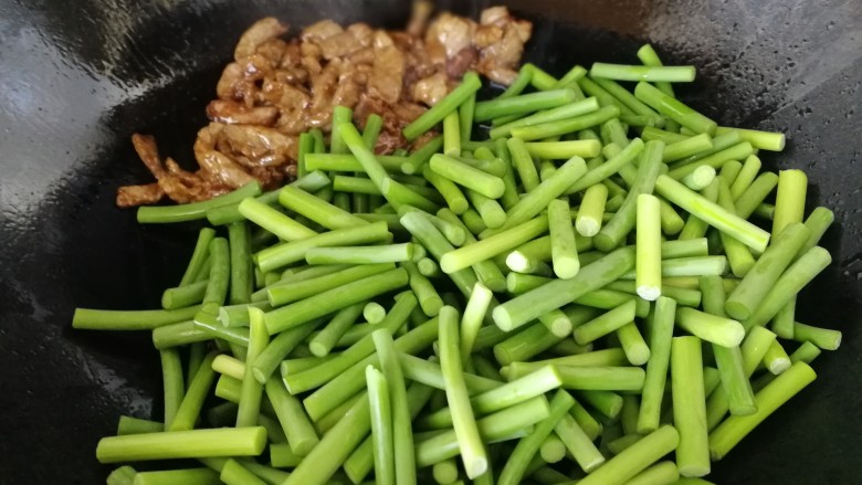 蒜苔炒牛肉,牛肉推到锅的一侧,倒入蒜薹段,急火翻炒均匀。