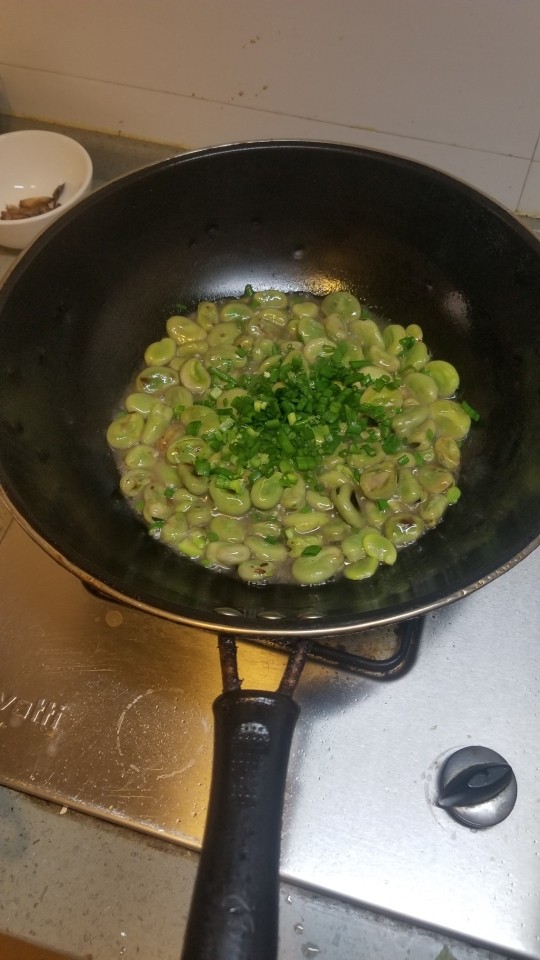 葱油蚕豆,焖煮7分后,看蚕豆开口就好,放入盐糖,葱叶末大火翻炒
