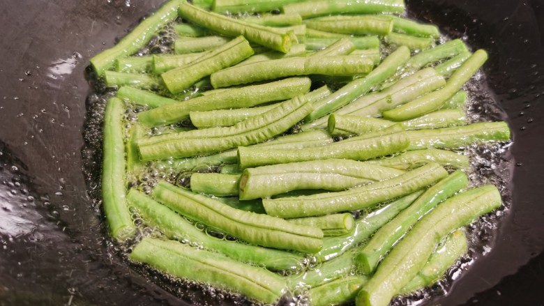 豇豆烧茄子,锅里放油多一点,放入豇豆过油炸软。不用担心太过油腻,豇豆油炸时不太怎么吸油。