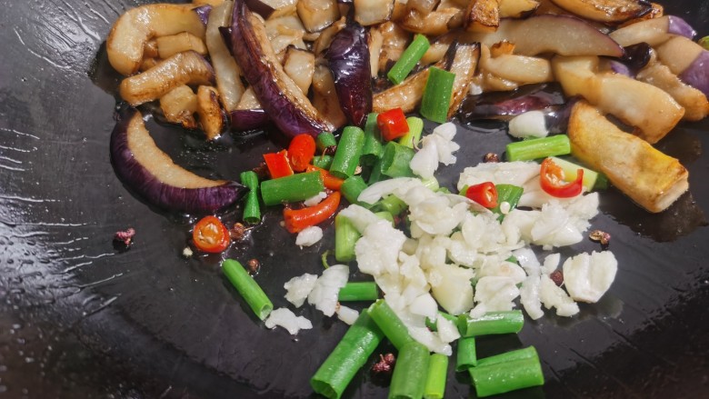 豇豆烧茄子,当茄子煎软后,放入葱、蒜、辣椒煸炒出香味。