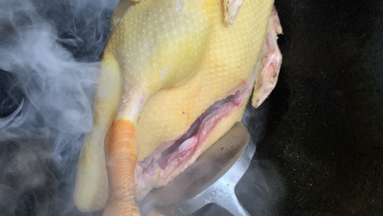 白切鸭,一手拿鸭爪一手用铲子把鸭子大腿部分来回摩擦锅面,让表面出油而焦黄。