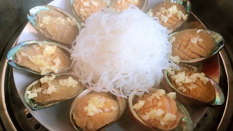 蒜蓉粉丝蒸鲍鱼,少量蒜末撒在鲍鱼肉上,把盘子放在笼屉里,上锅蒸5分钟