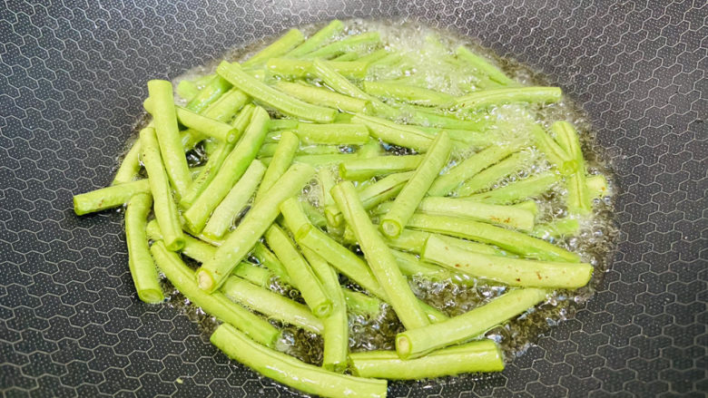 豇豆烧茄子,锅中加入食用油,可以多一些,加热至五成热,倒入豇豆小火慢炸,炸至微微皱皮即可