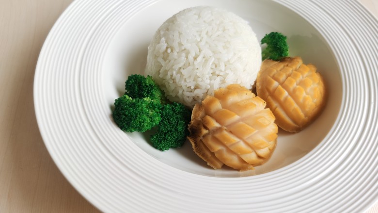 鲍鱼捞饭,将碗里的米饭倒扣到盘中,把焯熟的鲍鱼也摆入盘中,再放上几朵西兰花,最后将料汁浇到鲍鱼上即可。
