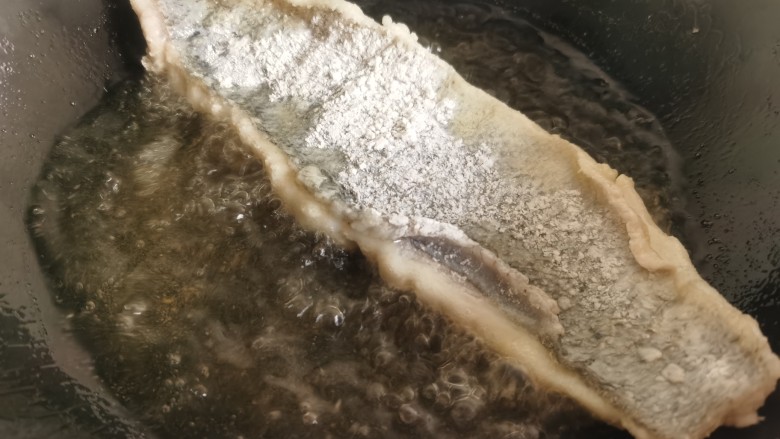 糖醋鲈鱼,锅里放油烧热,将鱼肉朝下放入油锅里炸制。