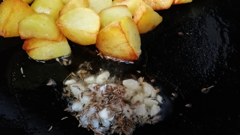 香酥小土豆,把土豆推到锅的一边,放入切好蒜末和孜然粒,用锅里剩余的油小火炒香。