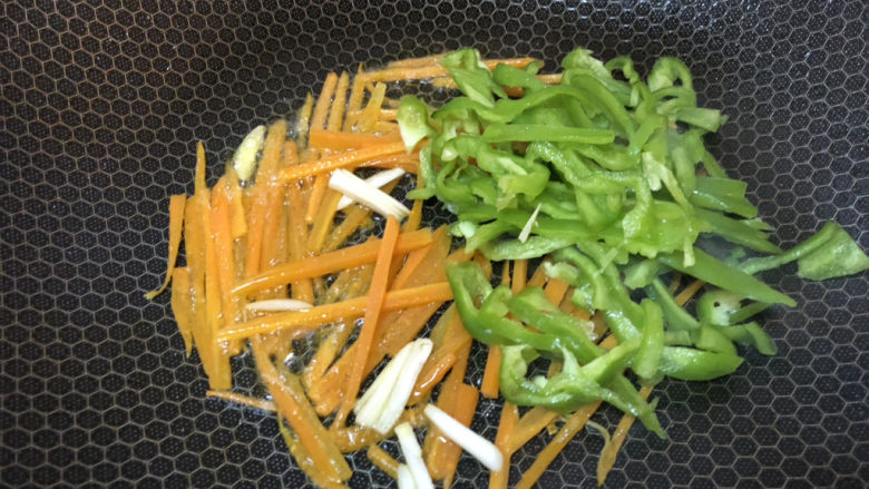 青椒炒腐竹,锅内加入油,先把蒜、胡萝卜、青椒倒入翻炒