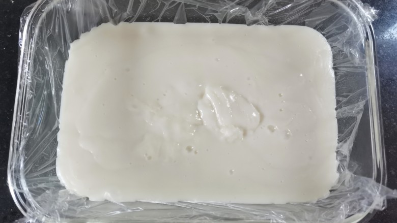 炸奶冻,取一个长方形的碗，里面铺上一层保鲜膜，倒入熬好的牛奶，用铲子铲平，放入冰箱冷冻两小时，