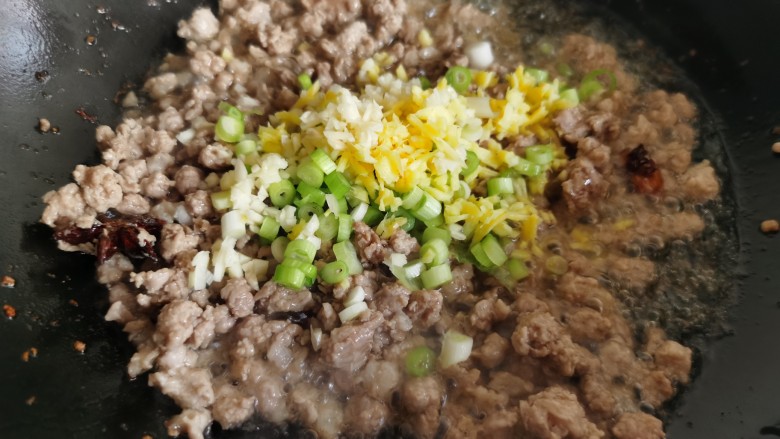 老北京炸酱面,肉煸炒至变色,加入姜、蒜和一半的葱花翻炒。葱花不要都加进去,留下一半备用。