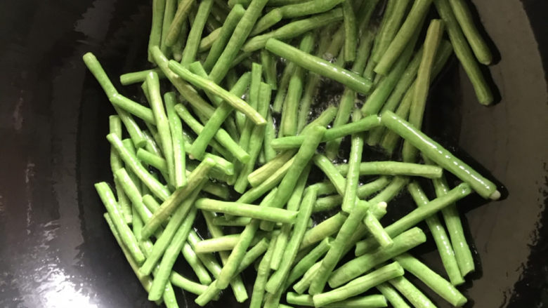 干煸豇豆,趁凉油时把豇豆放入下锅,小火慢慢煸,煸至豇豆表面起皱,这步比较费时费火,要有耐心。