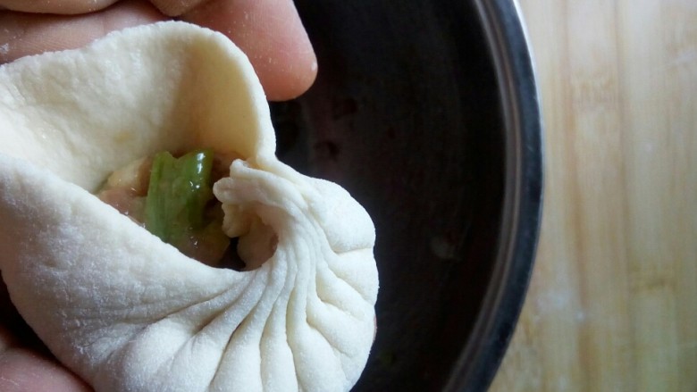 牛肉圆葱生煎包,右手大拇指捏紧面皮不动,食指捏包子褶,左手旋转包包子。