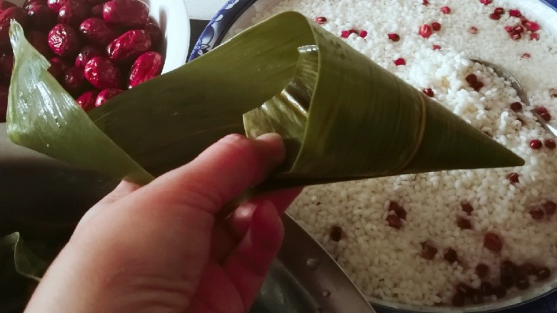 红豆粽子,取一片粽叶,剪掉根部,挽成三角漏斗形状。
